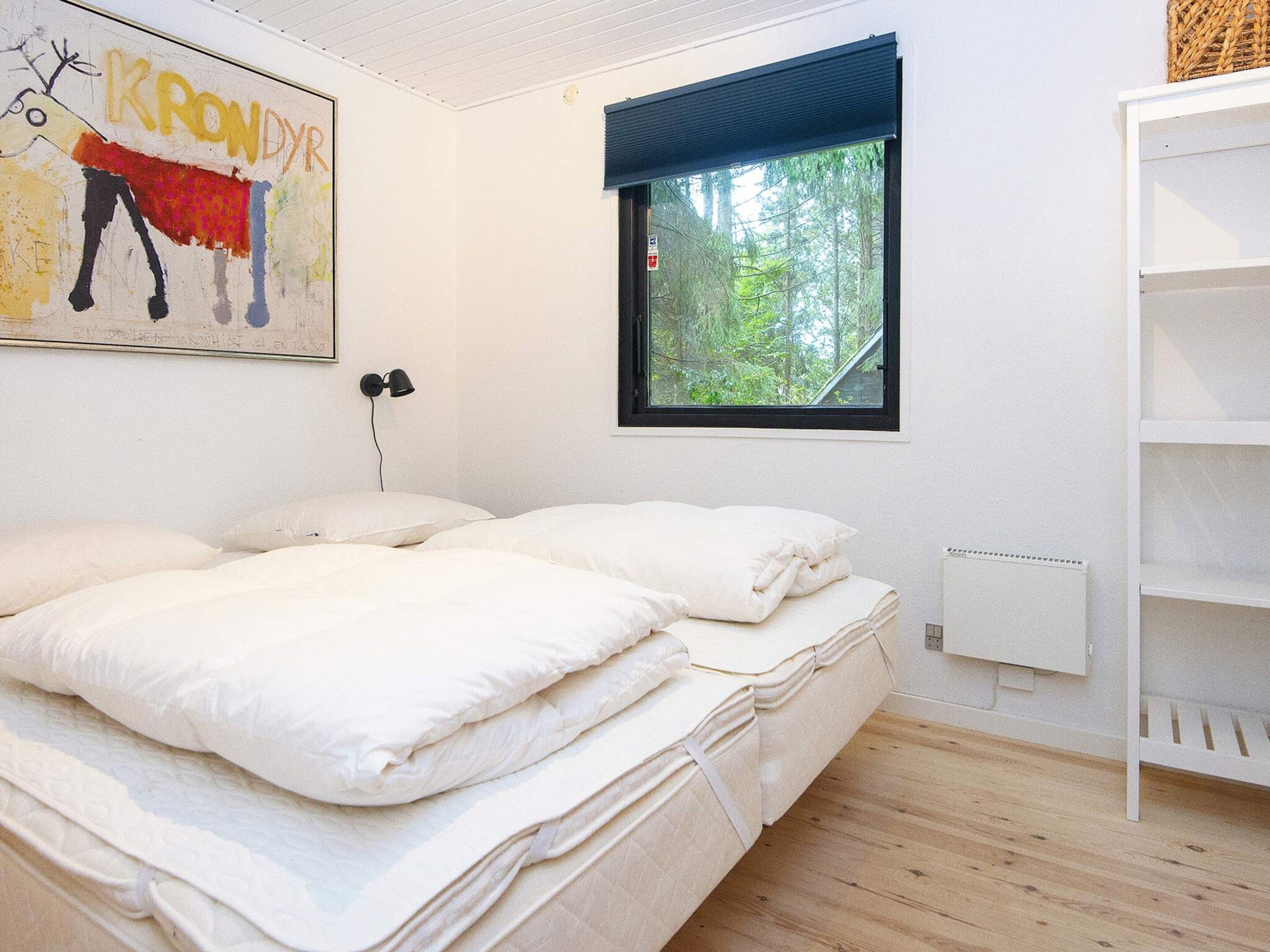 A bedroom with a bed, a window with a view of trees, a wall with a painting, and a white shelf unit.