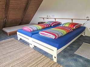 A small, cozy room with a sloped ceiling, a single bed with colorful striped bedding, a bench, and a small table.