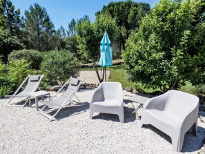Un jardin avec des chaises longues en plastique blanc et un parasol bleu.