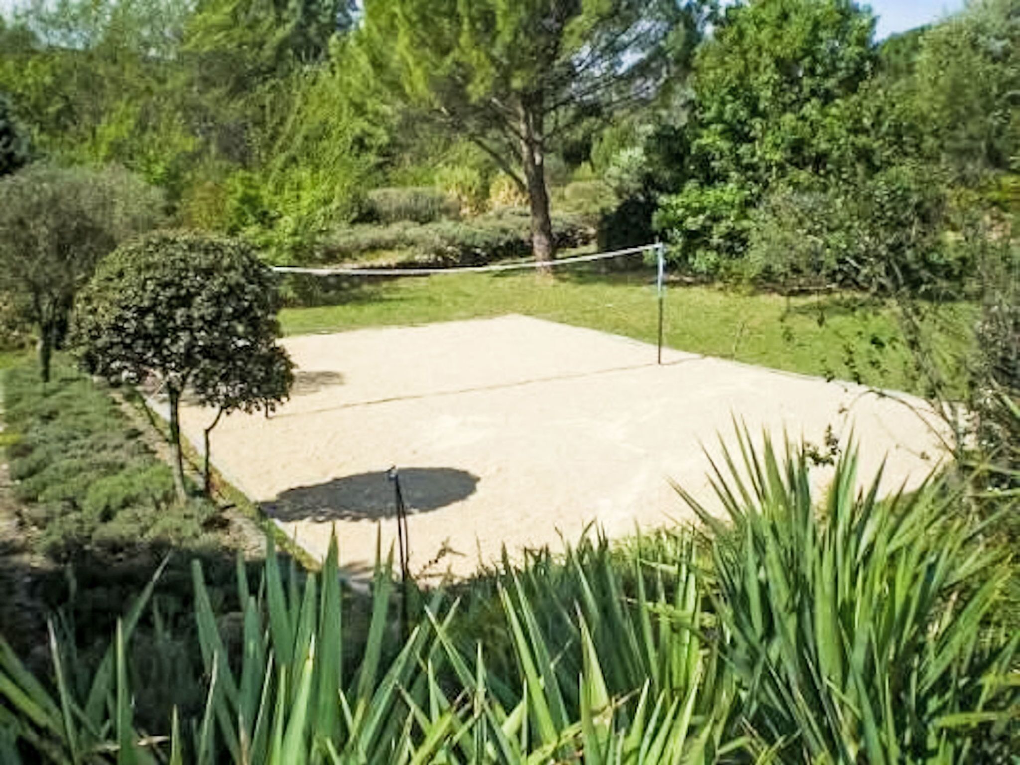 A tennis court with a net, surrounded by greenery and trees.