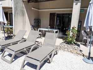 Une terrasse avec des chaises longues, une table et des chaises, une petite plante et l’entrée d’un bâtiment.