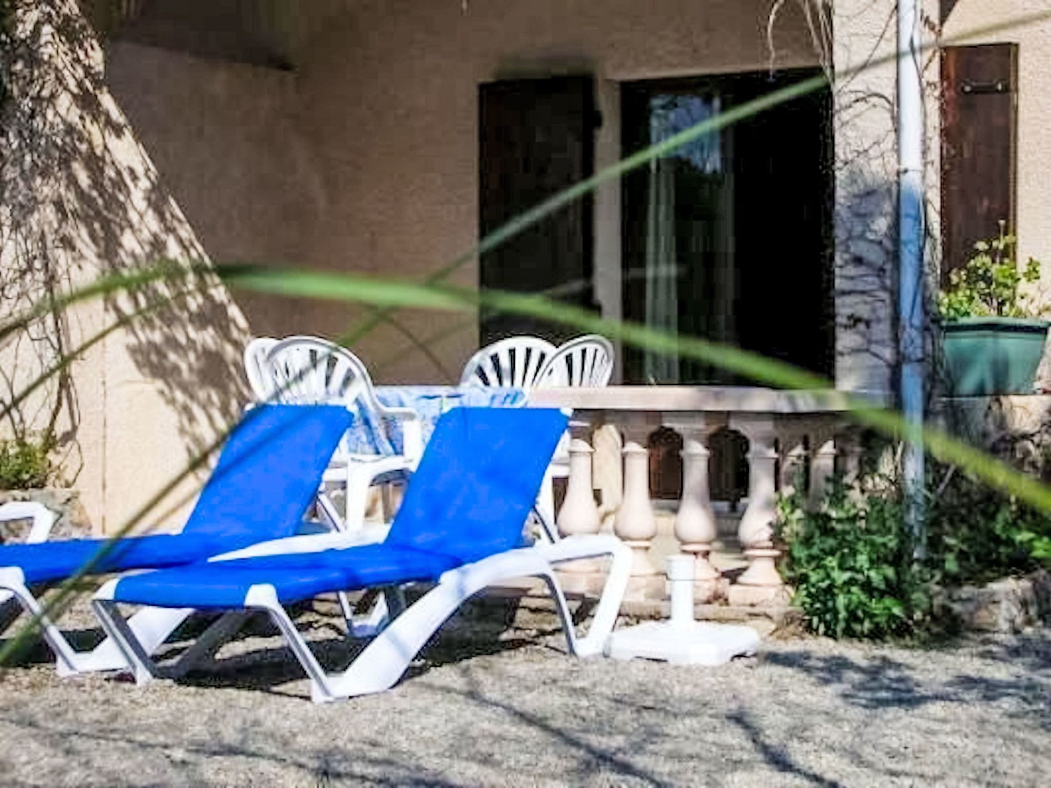 A patio with two blue lounge chairs and a table, a balustrade, and a building in the background.