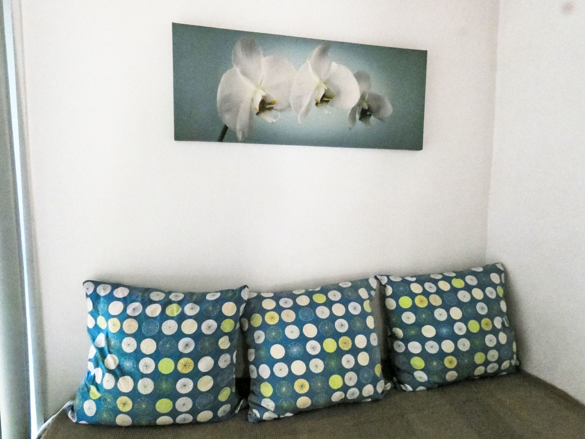 A room with a white wall, a framed picture of white flowers, and a sofa with polka-dotted cushions.