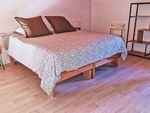Ein Bett mit einem gemusterten Überwurf, zwei Kissen und einem hölzernen Gestell.