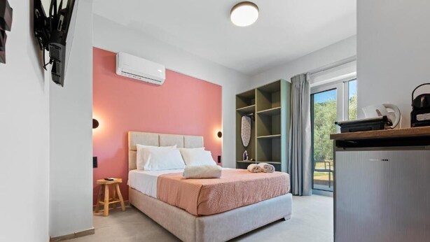 A bedroom with a bed, a small stool, a wardrobe, and a kitchenette. - Robin's | Red suite (Lefkada)