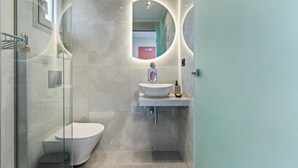 A modern bathroom with a glass shower enclosure, a white toilet, and a pedestal sink with a mirror above. - Robin's | Red suite (Lefkada)