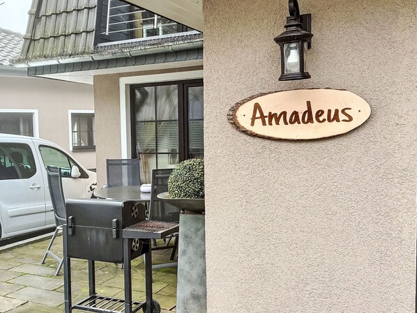 Ein Haus mit Grill, einem Auto und einem Schild mit der Aufschrift 'Amadeus'.