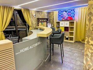 Ein Empfangsschalter mit gebogenem Design, eine Theke und ein Stuhl. An der Wand ist ein Fernseher angebracht, der eine Person zeigt.