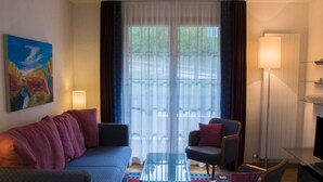 A modern hotel room with a sofa, armchair, glass coffee table, and a painting on the wall.