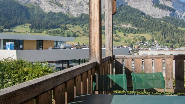 A wooden balcony with a view of mountains and a town.