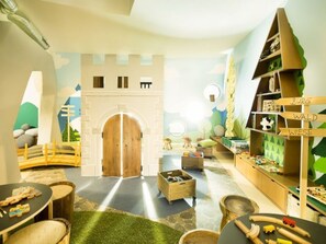 A children's playroom with a castle-themed play area, including a wooden archway, play tables, and a bookshelf labeled 'BURG WALD WIESE'. - Hapimag Resort Flims, (Flims Waldhaus), 2629 by Interhome (Flims)