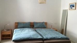 Et soveværelse med en seng, to sengeborde, en sengetavle, en pendel og et spejl på væggen.