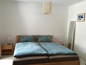Ein Schlafzimmer mit einem Bett, zwei Nachttischen, einer Nachttischlampe, einer Pendelleuchte und einem an der Wand befestigten Spiegel.