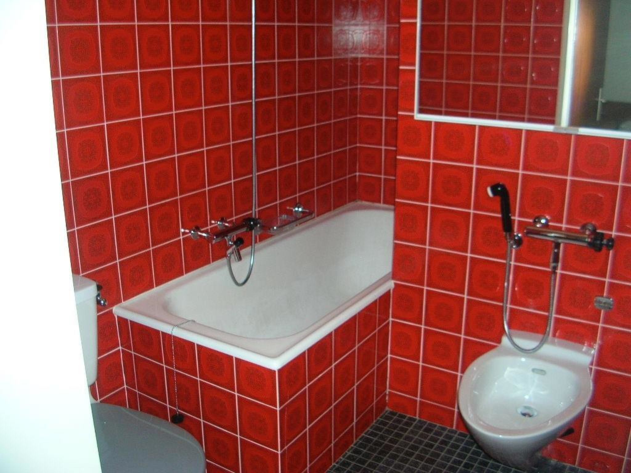 A bathroom with red tiled walls, a white bathtub, and a white toilet.