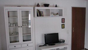Et værelse med et hvidt skab med glasdøre, et hvidt møbel med tv og radio, samt et mønstret tæppe på gulvet.