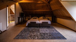 Une chambre avec un plafond en pente, un lit double, une petite table de chevet, une lampe et un tapis à motifs.