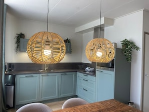 A modern kitchen with light blue cabinets, a wooden dining table, and two large woven pendant lights. - Oranjezon B by Interhome (Vrouwenpolder)