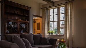 Un salon avec un canapé, un meuble en bois, une fenêtre avec des rideaux et un vase rempli de fleurs.