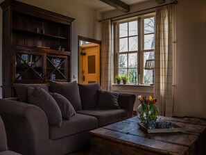 A living room with a sofa, a wooden cabinet, a window with curtains, and a vase with flowers. - Oranjezon B by Interhome (Vrouwenpolder)