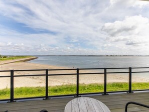 Blick von einer Terrasse auf einen Strand mit Sand und ruhigem Gewässer.