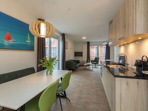 Une cuisine moderne avec un plan de travail en bois, un coin repas avec des chaises vertes et un tableau représentant des voiliers accroché au mur.