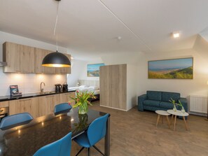Eine moderne Küche mit Holzschränken, einem Esstisch mit blauen Stühlen, einer Couch und einem Landschaftsbild.
