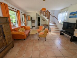 Ein Wohnzimmer mit einer Couch, Sesseln, einem Fernseher, einer Treppe und einem Holzschrank.