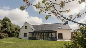 Een modern huis met een ruime glazen conservatorium, een schuin dak en een verzorgd gazon.