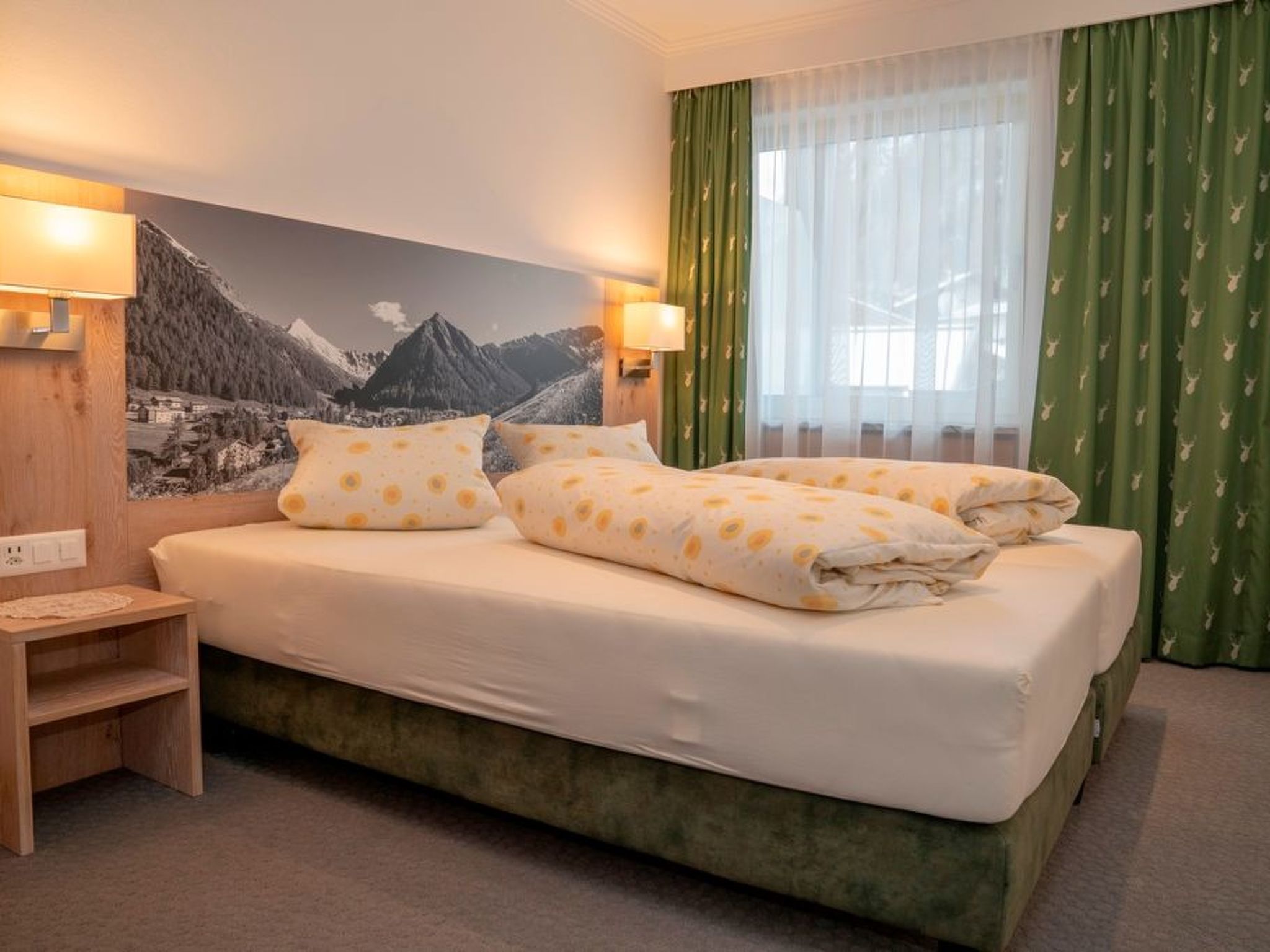 Een hotelkamer met een bed, een nachtkastje, een wandlamp en een raam met gordijnen.