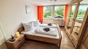 Un lit en bois avec du linge de lit blanc, une table de chevet avec une lampe et une vue sur la verdure à l’extérieur.