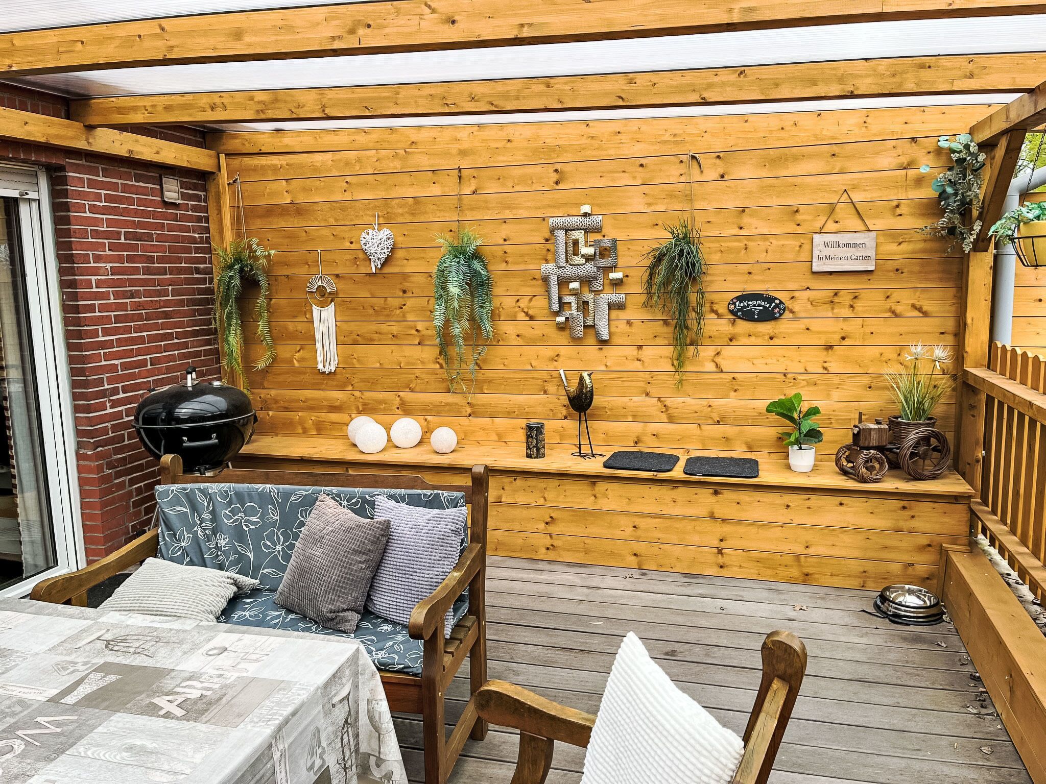 A wooden deck with a barbecue grill, a cushioned seating area, and various decorative items.