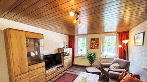 Un salon chaleureux avec un plafond en bois, un téléviseur à écran plat, un meuble en bois, un canapé, une table avec une bougie et une plante en pot.