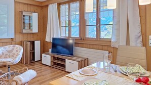 Een kamer met houten lambrisering, een televisie, eettafel, stoelen en een rieten mand.