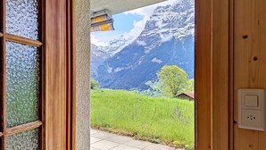 Een houten deur die leidt naar een kamer met uitzicht op een bergachtig landschap.