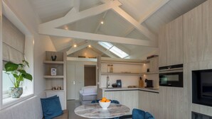 A modern kitchen with a built-in oven, a dining area with a round table and blue chairs, and a living area with a sofa and a plant. - Lepelaar by Interhome (Domburg)