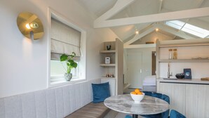 A modern kitchen with a built-in oven, a dining area with a round table and blue chairs, and a bench with a potted plant. - Lepelaar by Interhome (Domburg)