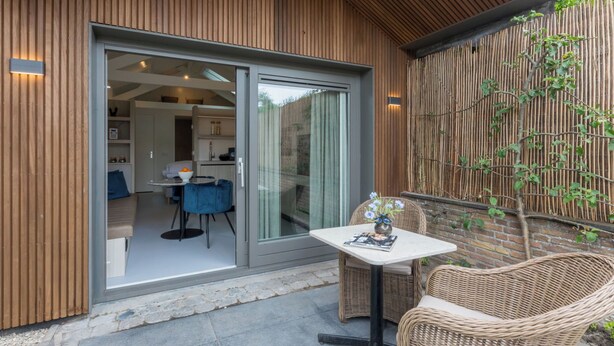 A modern patio with a glass door leading to a kitchen, wicker furniture, and a stone pathway. - Lepelaar by Interhome (Domburg)