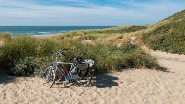 Una bicicletta parcheggiata su un sentiero sabbioso, con dune e l'oceano sullo sfondo.