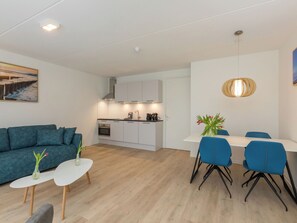 Ein modernes Wohnzimmer mit einer Couch, einem Esstisch mit Stühlen, einer Küchenzeile und einer Pendelleuchte.