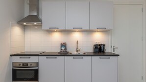 Una cucina moderna con mobili bianchi, un piano di lavoro nero, forno integrato, cappa aspirante e macchina per il caffè.