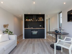 Eine moderne Küche mit Einbaugeräten, ein Essbereich mit rundem Tisch und Stühlen sowie eine Sitzecke mit einer Couch.