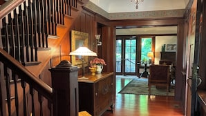 A wooden staircase with a lamp, a wooden bench, a cabinet, and a view into a room with a door and a window.