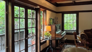A room with a piano, a sofa, a table with a lamp, and a view through large windows.