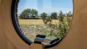 Ein Fenster mit Blick auf ein Feld, Bäume und eine entfernte Landschaft.