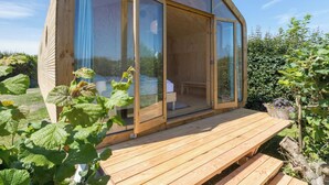 Eine Holzhütte mit einer großen Schiebeglastür, einer Holzterrasse und einem Garten mit Pflanzen.