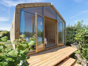 A wooden cabin with a large sliding glass door, a wooden deck, and a garden with plants. - Tiny House Rustepolder by Interhome (Vrouwenpolder)
