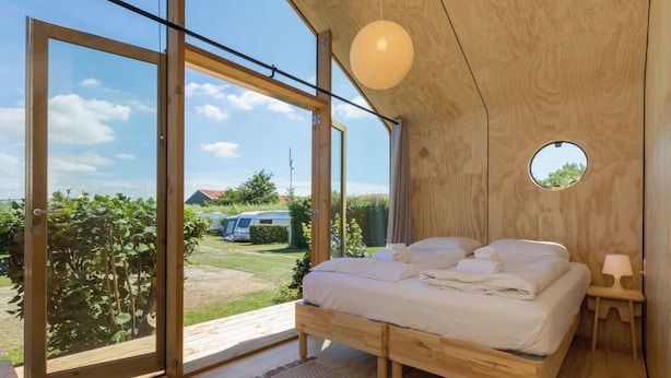 Ein Schlafzimmer mit großem Fenster, einem Bett, einem runden Spiegel und einem kleinen Tisch.
