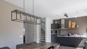 Une cuisine moderne dotée d’un îlot central, d’un four encastré et d’un coin repas avec une table et des chaises en bois.