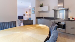 Eine moderne Küche mit Essbereich, ausgestattet mit einem runden Holztisch, grauen Polsterstühlen, Edelstahlgeräten und einem Einbauofen.