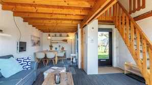 Een gezellig interieur met een houten plafond, een bank, een eethoek en een trap.